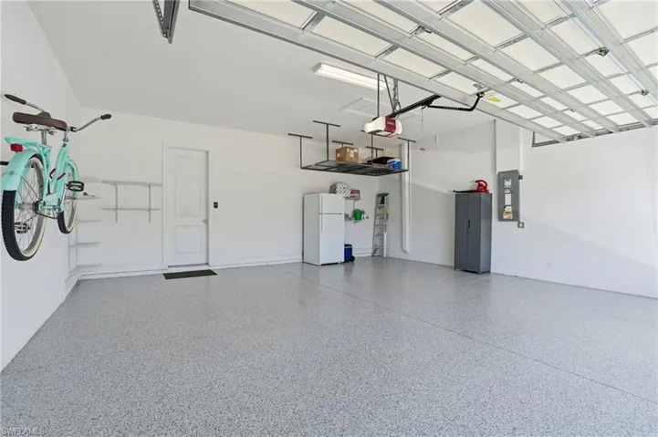 Garage with freestanding refrigerator, electric panel, and a garage door opener