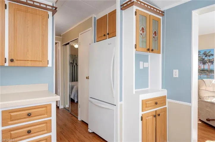 Kitchen with glass insert cabinets, crown molding, light countertops, freestanding refrigerator, and light wood-style floors