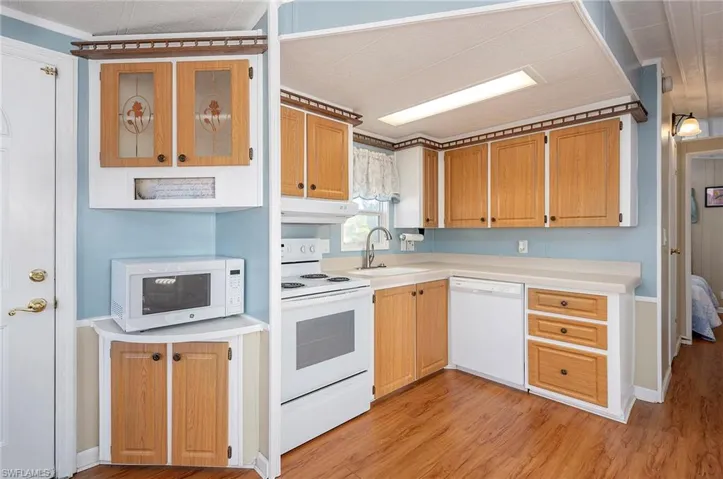 Kitchen featuring light countertops, a sink, light wood finished floors, under cabinet range hood, and white appliances