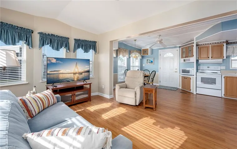 Living room with baseboards, ceiling fan, wood finished floors, and vaulted ceiling