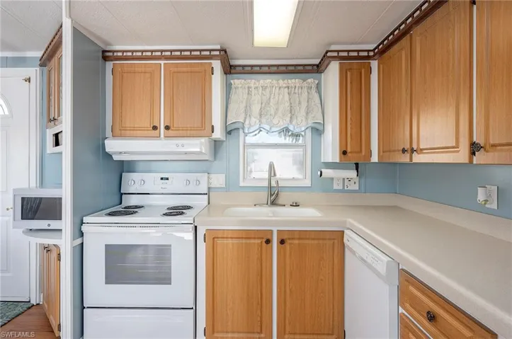 Kitchen with a sink, under cabinet range hood, white appliances, and light countertops