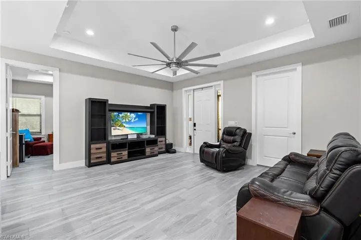 Living room with a ceiling fan, a raised ceiling, light wood-type flooring, and visible vents