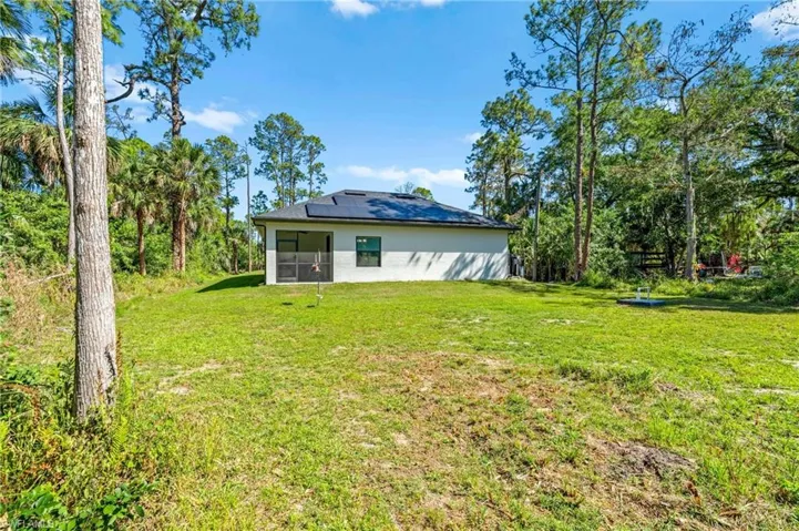 Back of property with solar panels, a sunroom, stucco siding, and a yard