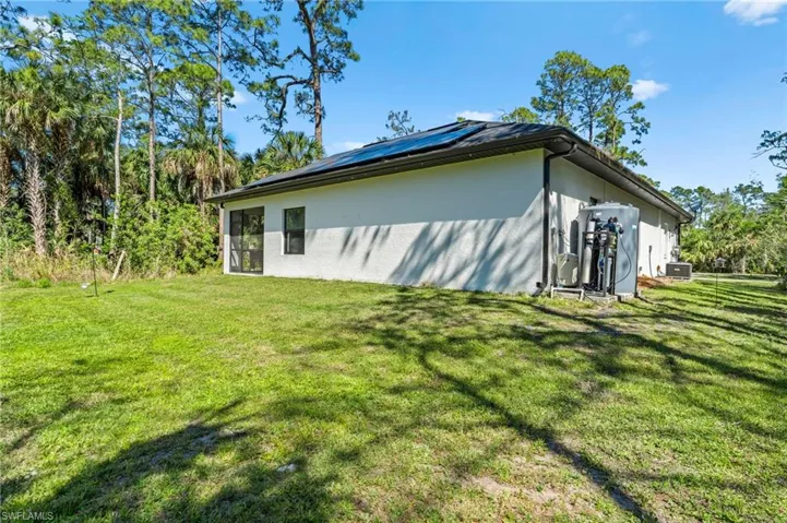 View of side of property featuring cooling unit, a lawn, stucco siding, and roof mounted solar panels