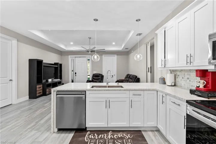 Kitchen with a raised ceiling, a sink, a ceiling fan, a peninsula, and appliances with stainless steel finishes