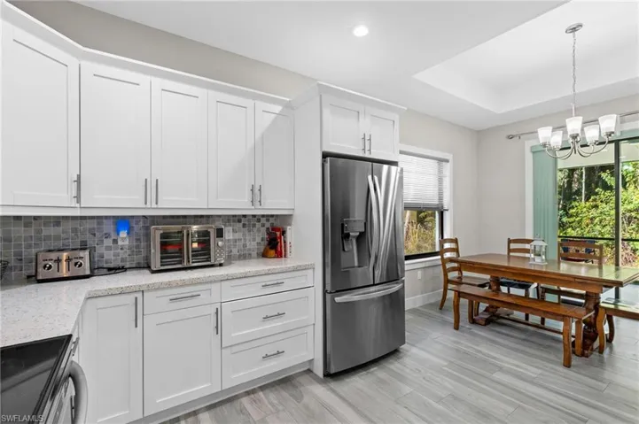Kitchen featuring white cabinets, a chandelier, tasteful backsplash, stainless steel refrigerator with ice dispenser, and stove
