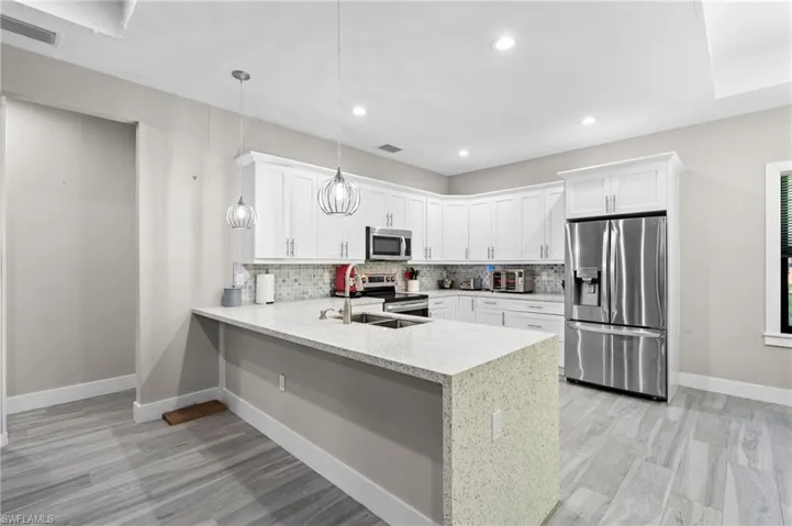 Kitchen with visible vents, a peninsula, stainless steel appliances, white cabinetry, and backsplash