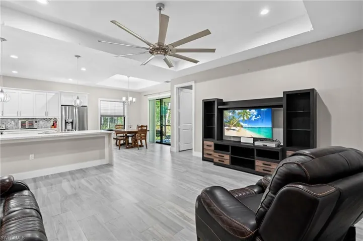 Living area featuring baseboards, recessed lighting, ceiling fan with notable chandelier, and a raised ceiling