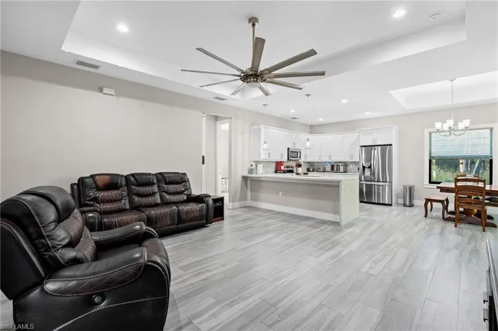Living room with a tray ceiling, light wood finished floors, baseboards, ceiling fan with notable chandelier, and visible vents