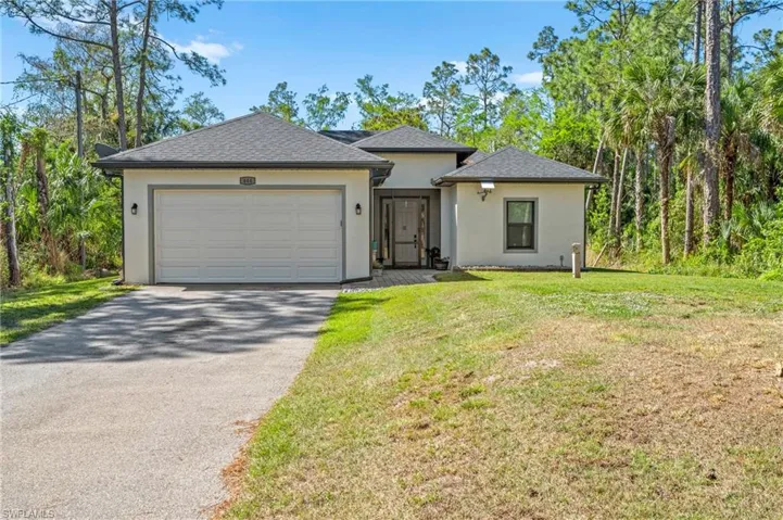 View of front facade with driveway, stucco siding, an attached garage, a front lawn, and a shingled roof