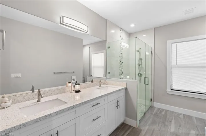 Bathroom featuring a stall shower, baseboards, double vanity, and a sink