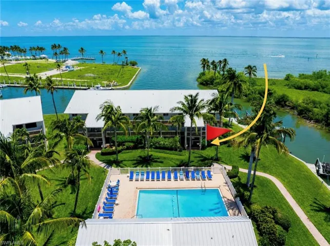 Waterfront residential complex featuring a swimming pool with deck chairs, multiple boat docks, mature palm trees, and direct access to open water