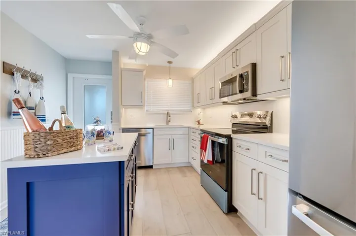 Bright kitchen featuring a blue island with a white countertop, white shaker cabinetry, stainless steel appliances, and wood-finish tile flooring