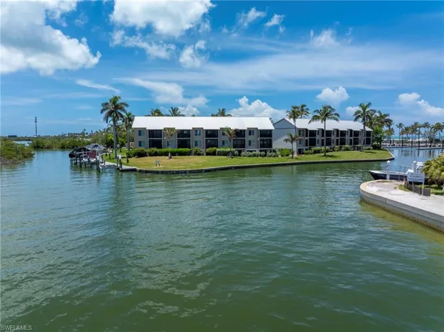 Waterfront multi-story buildings with balconies, surrounded by mature palm trees and green landscaping