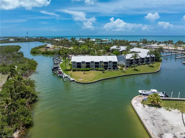 Waterfront building with multiple units, featuring private balconies, individual boat slips, surrounding green space, and palm trees