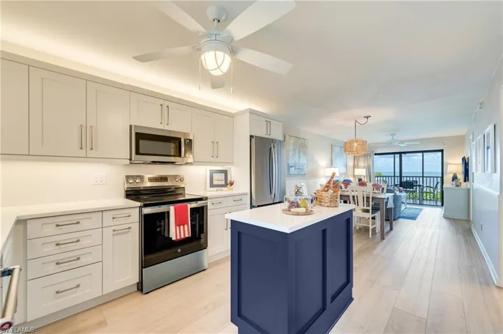 Open-concept kitchen featuring light-toned cabinetry, stainless steel appliances, a center island with a contrasting dark blue finish, and wood-finish flooring extending throughout the main living areas