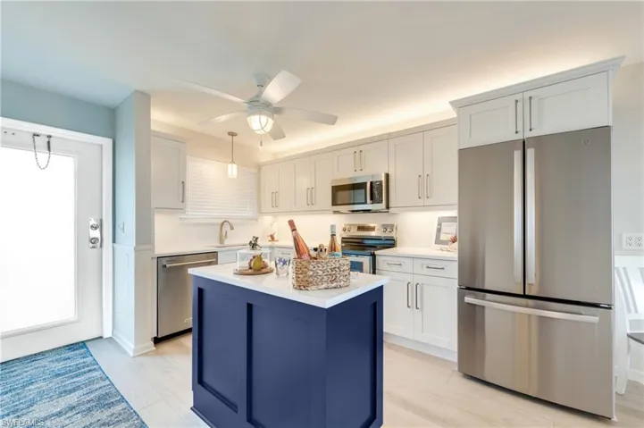 Kitchen featuring a contrasting blue island with a white countertop, stainless steel appliances, white cabinetry, recessed lighting, and light wood-finish tile flooring
