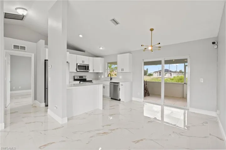 Kitchen with white cabinets, appliances with stainless steel finishes, lofted ceiling, and sink