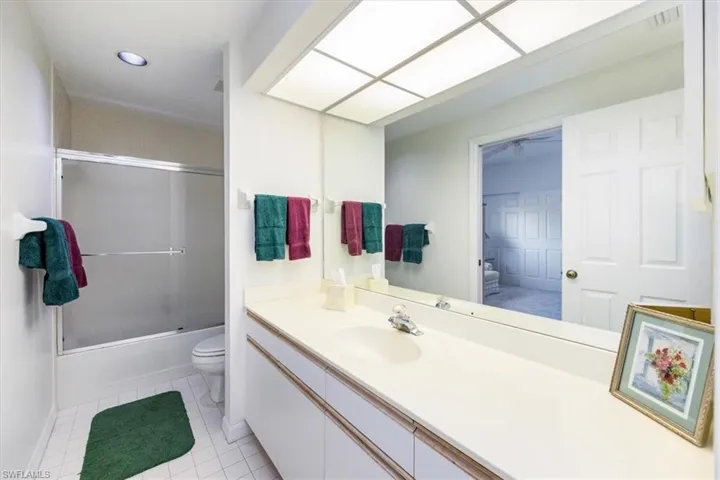 Full bathroom with toilet, vanity, tile patterned floors, and bath / shower combo with glass door