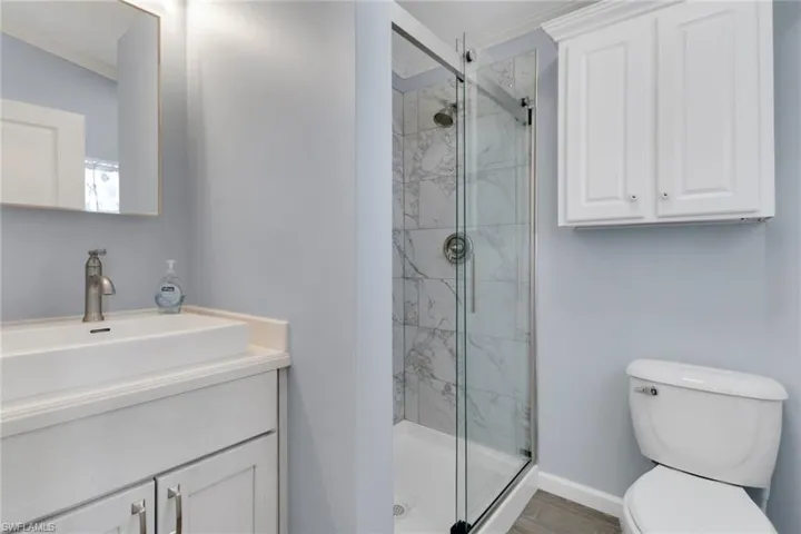 Bathroom with crown molding, a marble finish shower, vanity, and wood finished floors