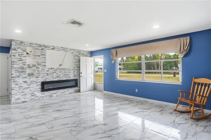 Unfurnished room featuring a tile fireplace, light marble finish floors, and an accent wall