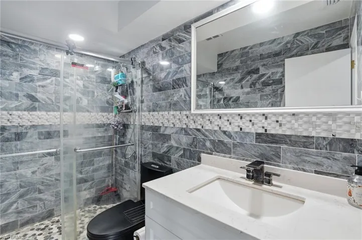 Bathroom with vanity, a shower stall, tile walls, and tasteful backsplash