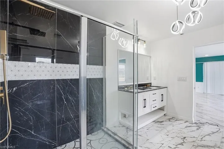 Bathroom featuring vanity, a marble finish shower, and light marble finish floors
