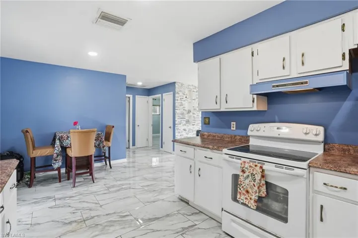 Kitchen with white electric range oven, dark countertops, white cabinetry, recessed lighting, and light marble finish floors
