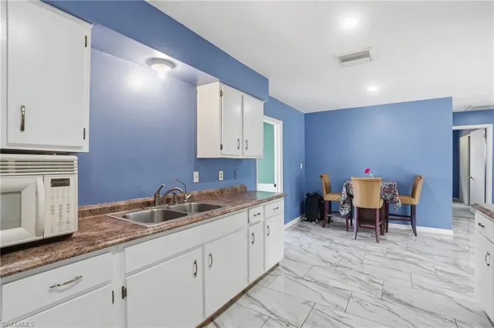 Kitchen featuring dark countertops, white microwave, light marble finish flooring, white cabinetry, and recessed lighting