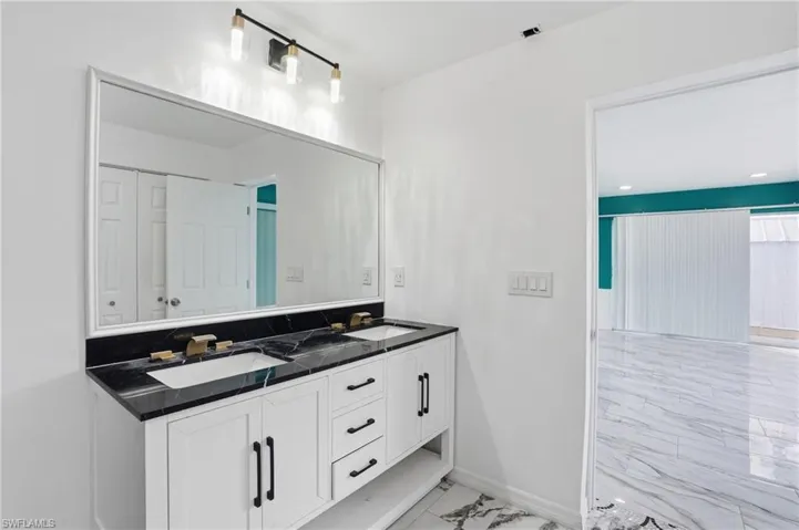 Bathroom with double vanity, light marble finish floors, and recessed lighting