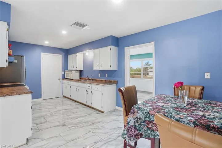 Kitchen featuring light marble finish flooring, white microwave, white cabinets, freestanding refrigerator, and dark countertops