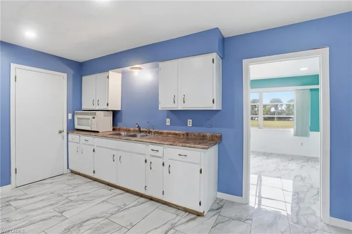 Kitchen with light marble finish flooring, white microwave, white cabinetry, and dark countertops