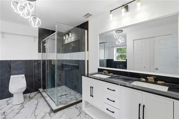 Full bath with double vanity, a closet, a marble finish shower, tile walls, and light marble finish flooring