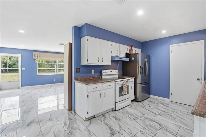 Kitchen with electric range, dark countertops, white cabinetry, light marble finish floors, and stainless steel fridge with ice dispenser