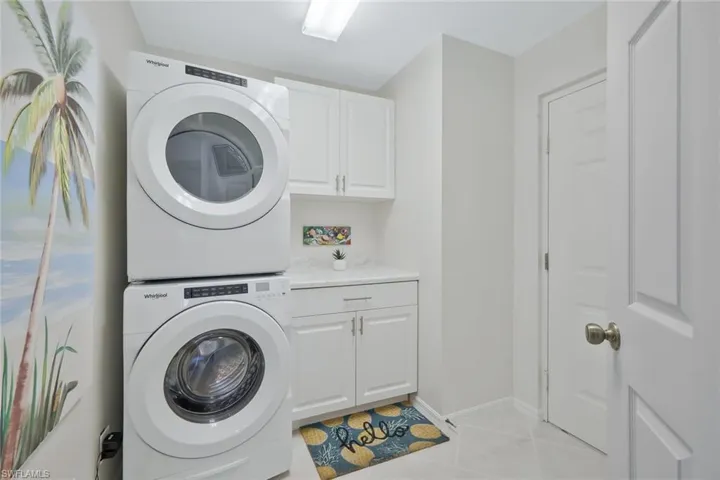 Laundry area with stacked washer and dryer, cabinet space, and light tile patterned floors