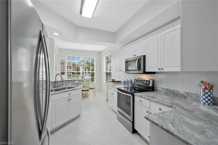 Kitchen with stainless steel appliances, white cabinets, light stone counters, backsplash, and decorative light fixtures