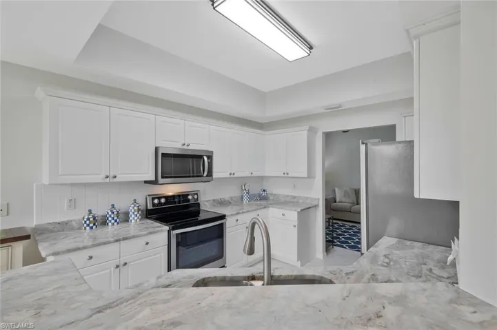 Kitchen featuring stainless steel appliances, white cabinetry, light stone countertops, and light tile patterned floors