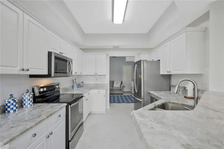 Kitchen with stainless steel appliances, white cabinets, a tray ceiling, light stone counters, and light tile patterned flooring