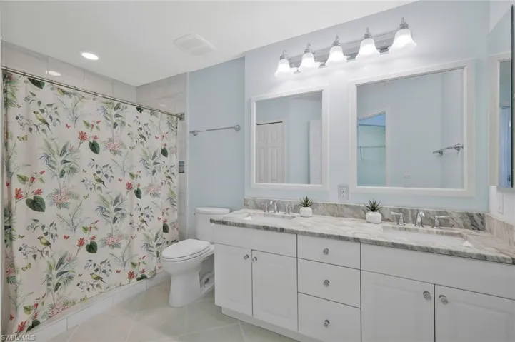 Full bath with double vanity, a shower with curtain, and light tile patterned flooring