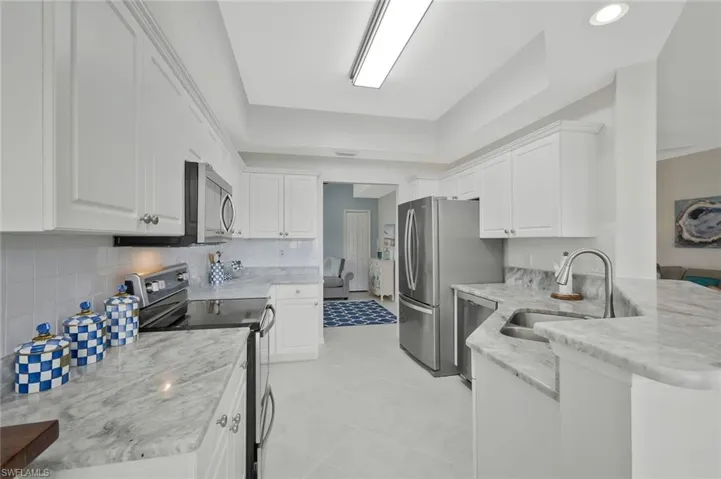 Kitchen featuring stainless steel appliances, a raised ceiling, white cabinets, a peninsula, and light stone counters