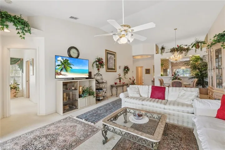 Carpeted living room with ceiling fan with notable chandelier and lofted ceiling