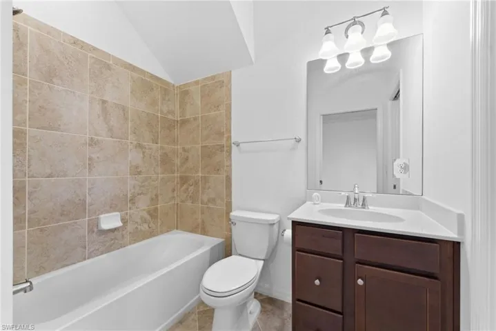 Bathroom with vanity, tub / shower combination, vaulted ceiling, and light tile patterned flooring
