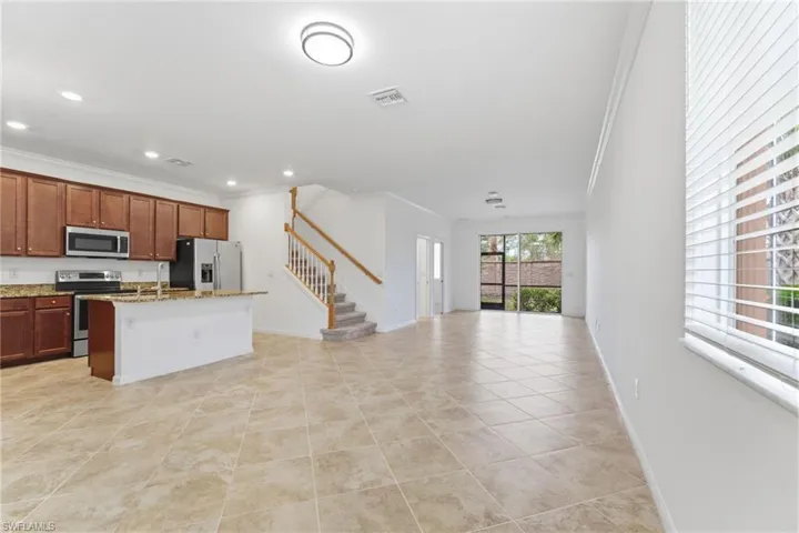 Kitchen with open floor plan, crown molding, stainless steel appliances, light stone counters, and a kitchen island with sink