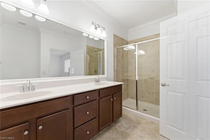 Bathroom featuring double vanity, a shower stall, crown molding, and light tile patterned floors
