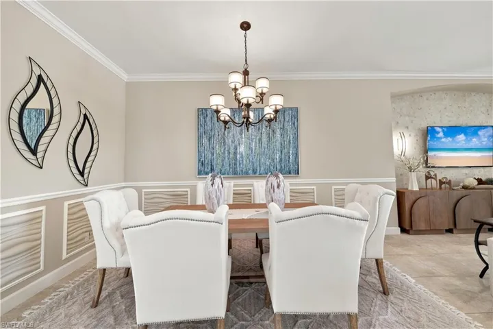 Dining area featuring crown molding, a multi-arm chandelier, and wainscoting details with textured panels