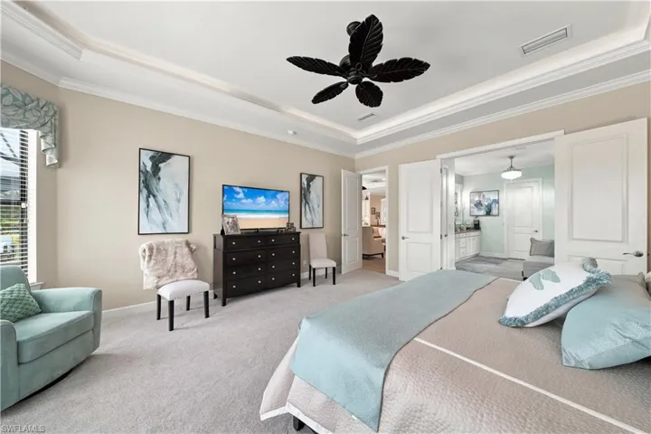 Carpeted bedroom featuring a tray ceiling with crown molding, a decorative ceiling fan, and light-toned wall paint