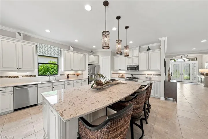 Open-concept kitchen featuring an expansive island with seating, white shaker cabinetry, stainless steel appliances, pendant lighting, and tile flooring