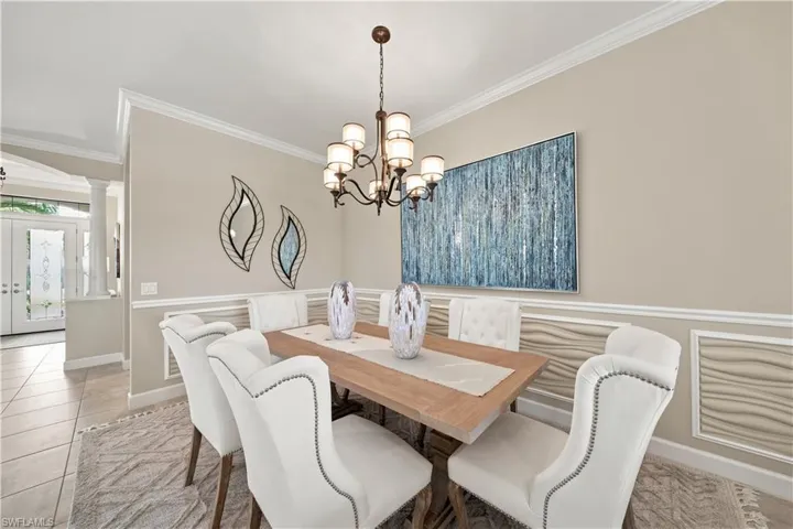 Dining area featuring a chandelier, decorative wall paneling, crown molding, and tiled flooring extending into an entry hall with double glass doors