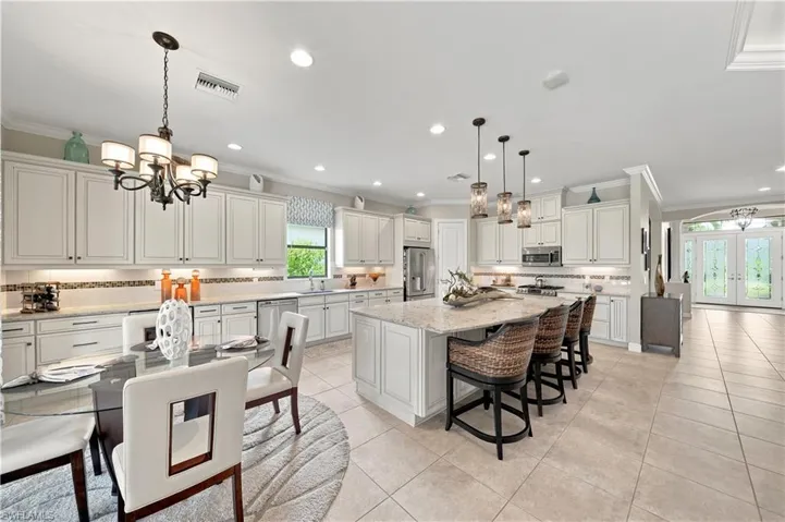 Open-concept kitchen and dining area featuring white shaker-style cabinetry, a large kitchen island with pendant lighting, stainless steel appliances, and tile flooring