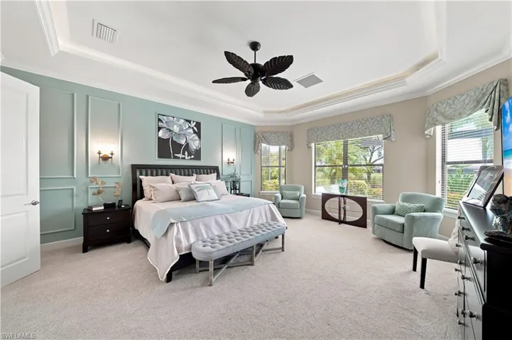 Spacious bedroom featuring light-colored carpeting, a tray ceiling with crown molding, and a dark-toned ceiling fan